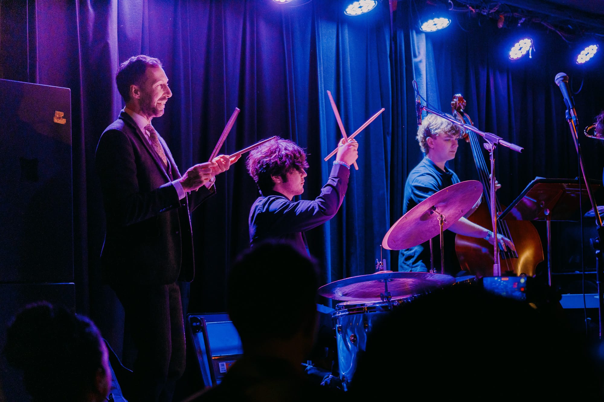 A drummer and young bassist perform together under blue and purple stage lights