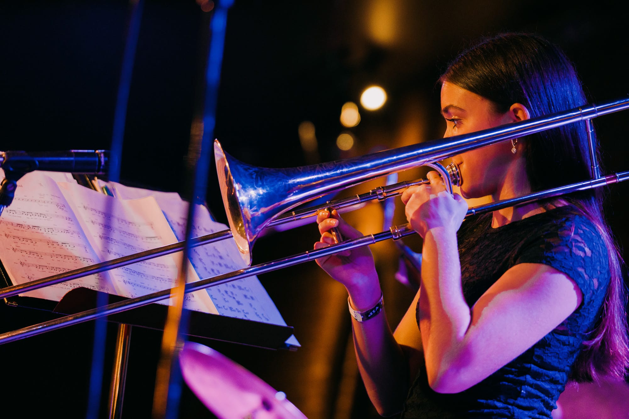 A young trombonist performs under vivid blue and amber stage lights
